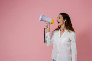 Confident woman using a megaphone against a soft pink background. Perfect for communication concepts.