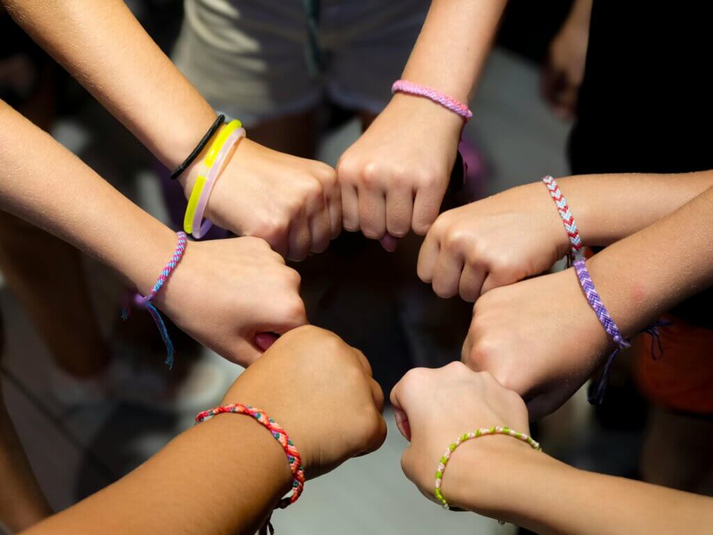 A diverse group of hands wearing colorful friendship bracelets in unity.