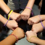 A diverse group of hands wearing colorful friendship bracelets in unity.