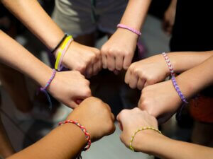 A diverse group of hands wearing colorful friendship bracelets in unity.