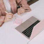 Businesswoman in a plaid jacket using a laptop and sticky notes for work planning.