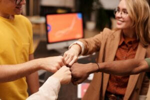 Group of colleagues fist bumping to celebrate teamwork and unity in a modern office setting.